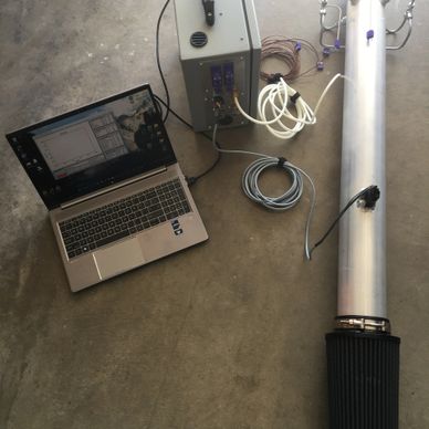 Laptop connected to a metallic cylindrical device with cables on a concrete floor.