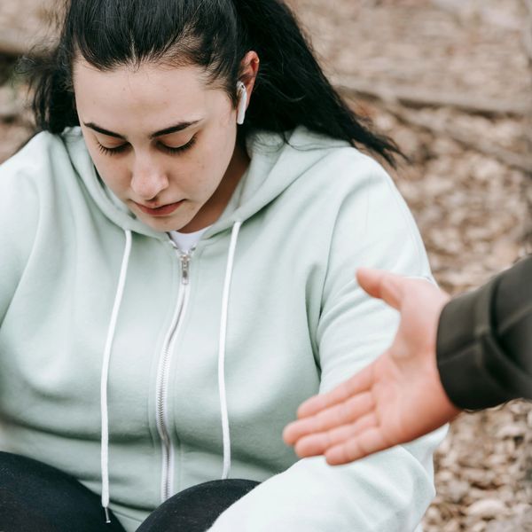 Someone sitting outdoors in a blue hoodie, while their friend reaches their hand out to them.  