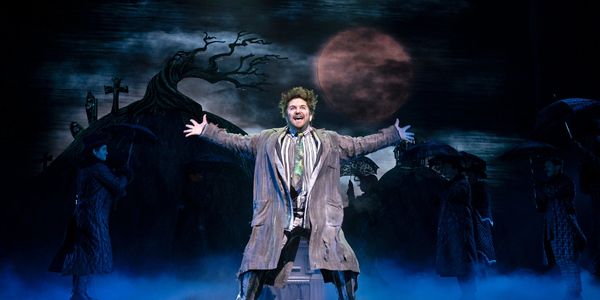 A theatrical scene with a man joyfully performing under a spooky moonlit sky.