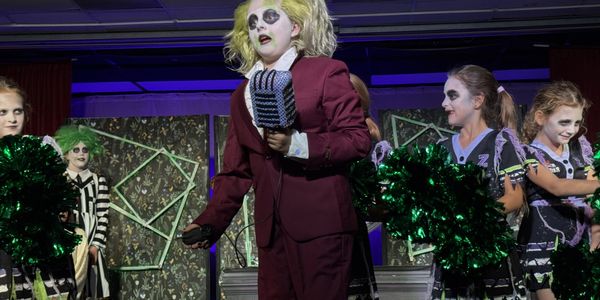 Children in Halloween costumes performing on stage with spooky makeup.