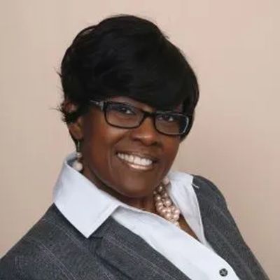 Professional portrait of a smiling woman in glasses and business attire.