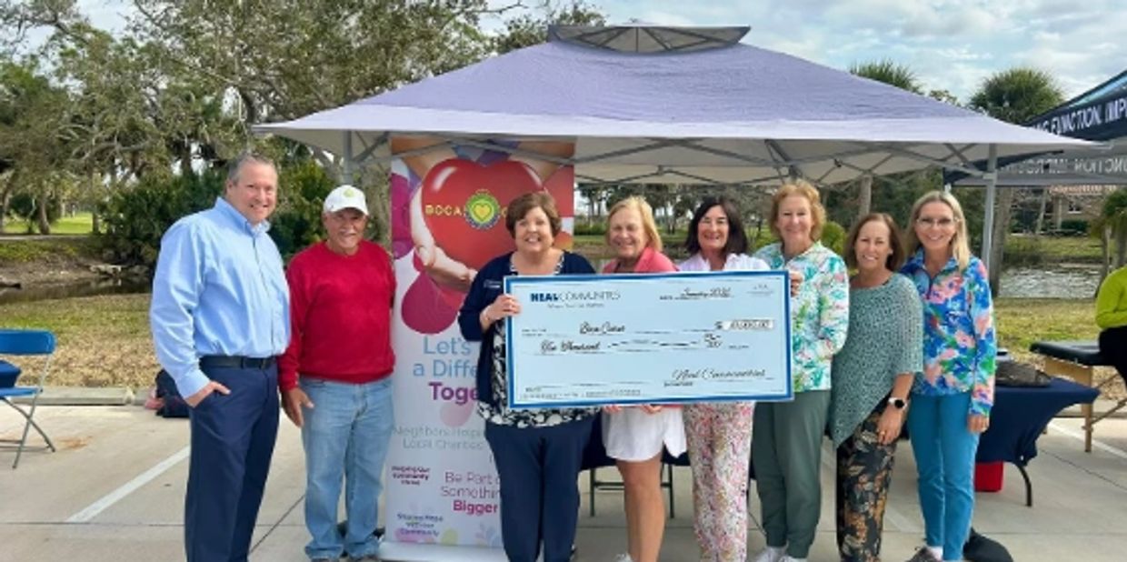 Group of people holding a large check under a tent outdoors.