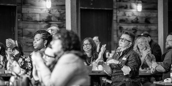 Black and white photo of people clapping at an indoor event.