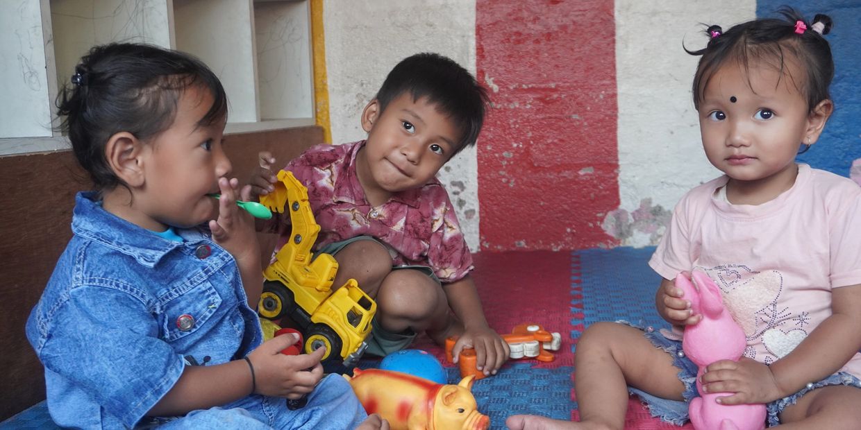 Three children playing with toys indoors on colorful mats.