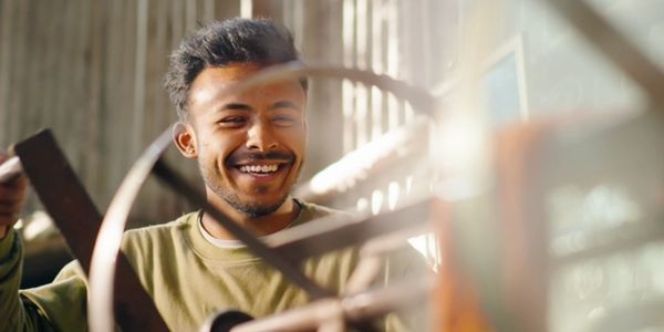 A man smiling while spinning dyed yarn with a tool in a workshop.