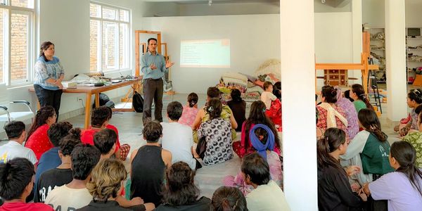 Man giving a presentation to seated weavers in a bright room