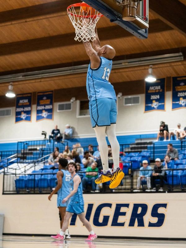 Basketball player in blue jersey mid-air dunking during a game in a gymnasium.