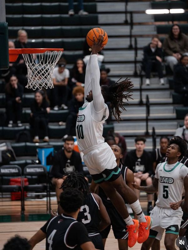 Basketball player in white jersey leaps for a slam dunk during a game.