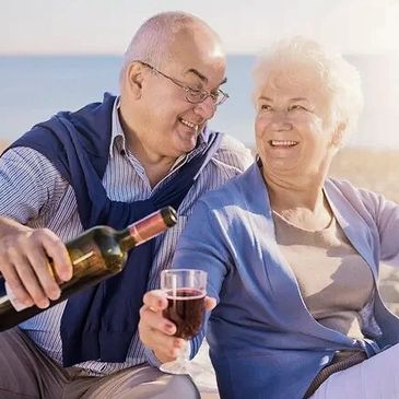 Senior husband and wife enjoying wine on the beach. Representing Reverse Mortgage, mortgages.