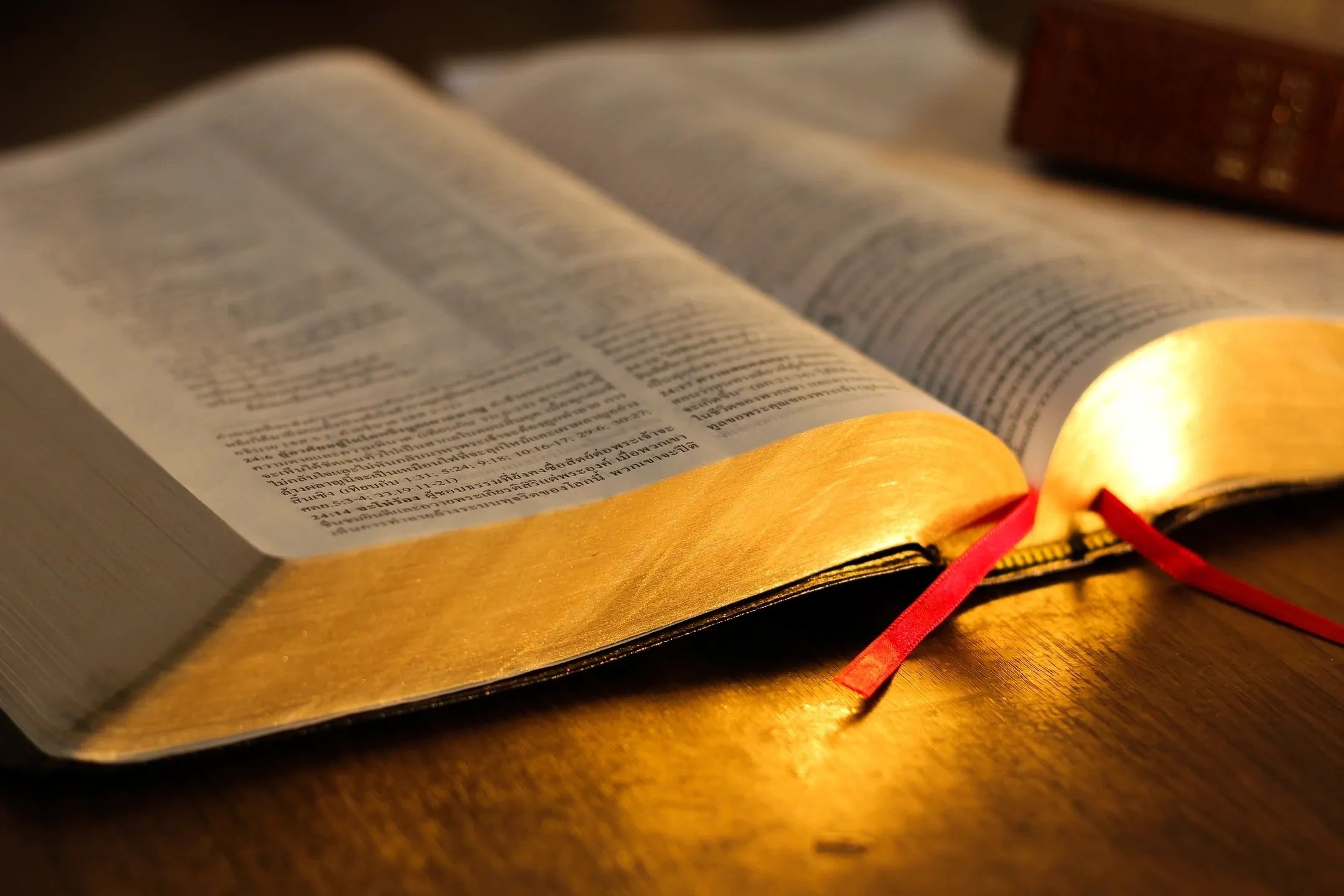 Open Bible with golden edges and red ribbons on a wooden surface.