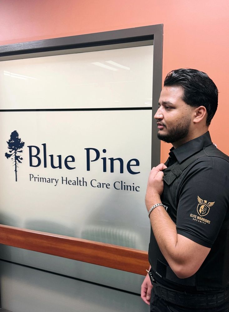 Security guard standing beside Blue Pine Primary Health Care Clinic sign.