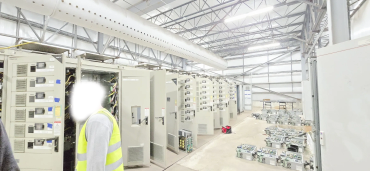 A worker inspecting electrical control panels in a large industrial facility.