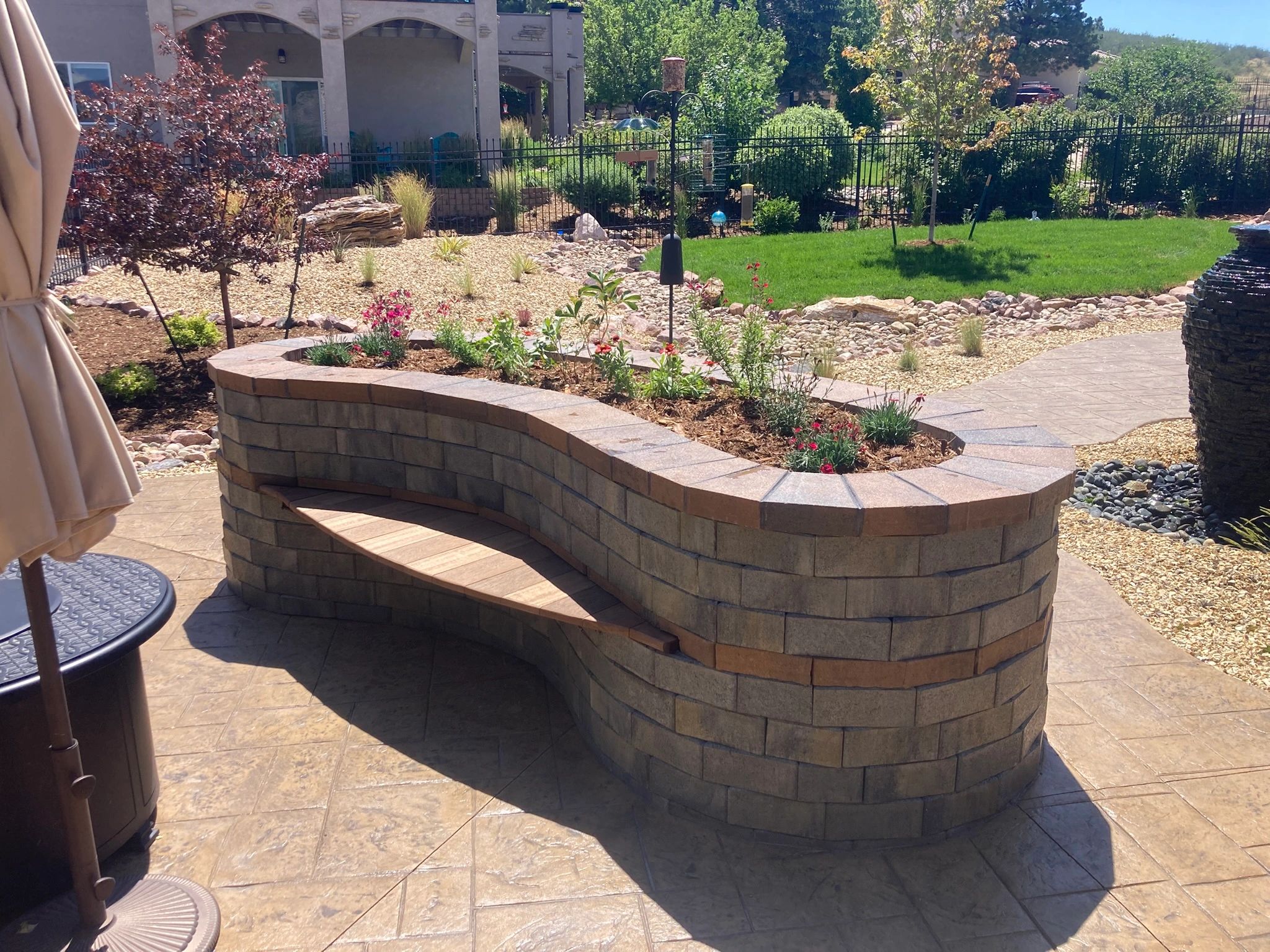 Curved stone bench with flowers in backyard garden.