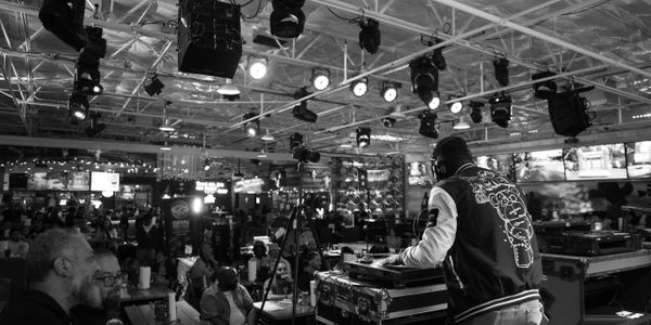 DJ performing live at a crowded indoor event venue with attentive audience.
