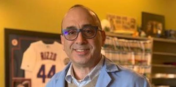 Smiling man wearing glasses and a blue jacket indoors.
