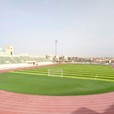 A bright, empty soccer field with a running track around it.