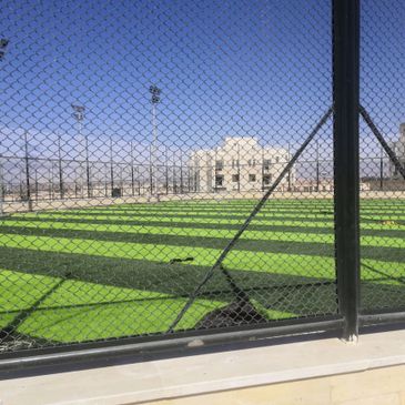Empty sports field enclosed by a chain-link fence on a sunny day.