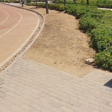 A dirt path runs between a paved walkway and green bushes beside a curved track.