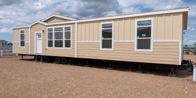 New beige modular home on gravel lot under cloudy sky.