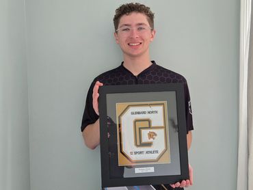 Young man holding a framed sports athlete award in front of a gray wall.