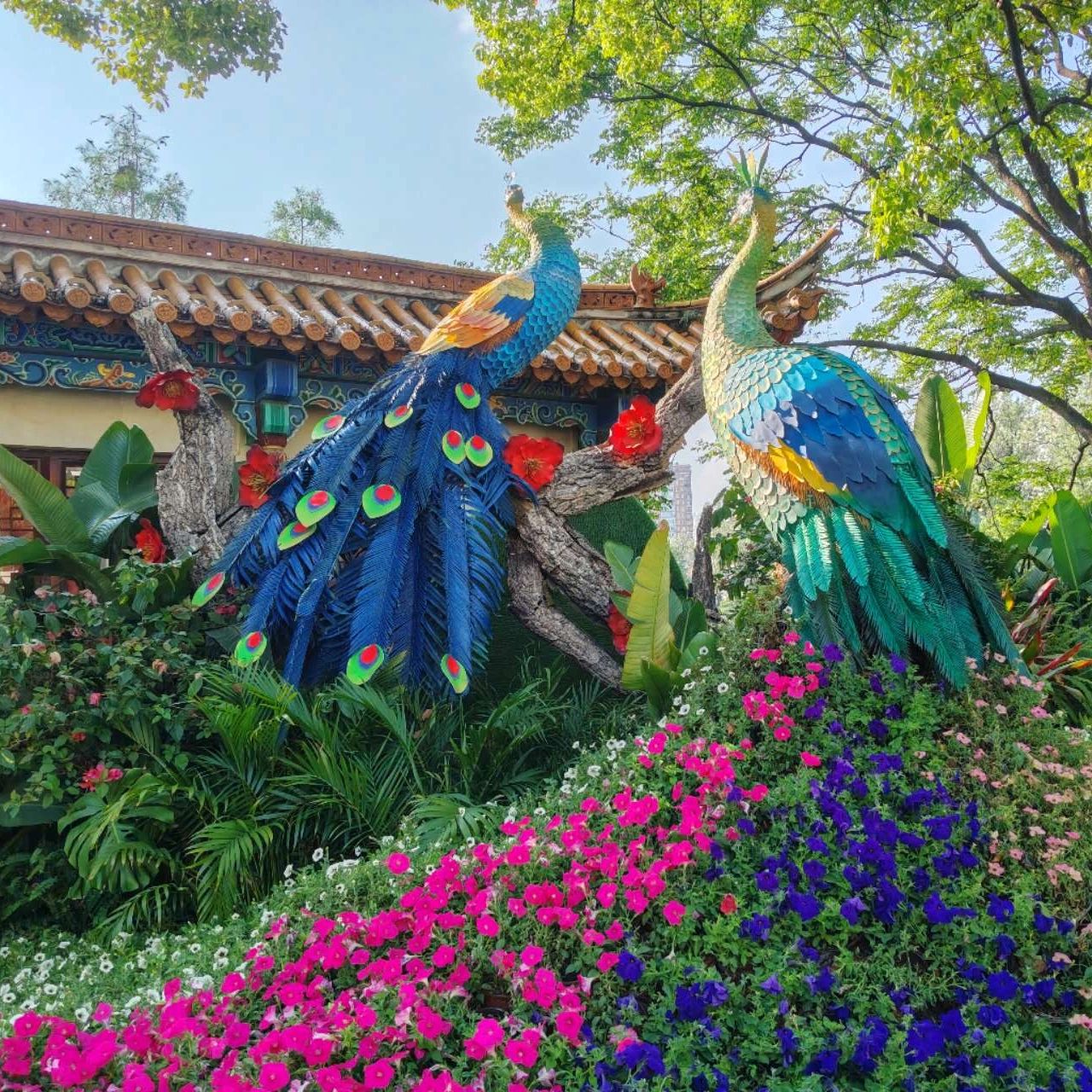 Colorful peacock sculptures amidst vibrant flowers and greenery.