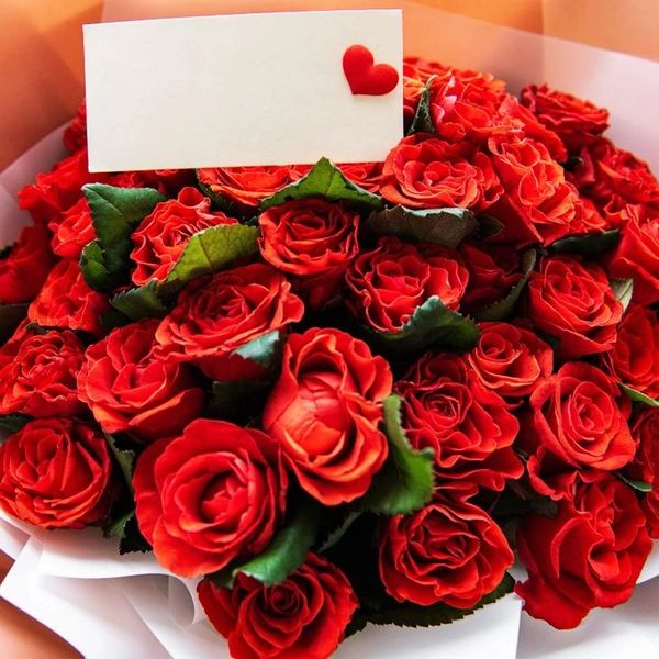 A bouquet of vibrant red roses with a small heart-adorned card.