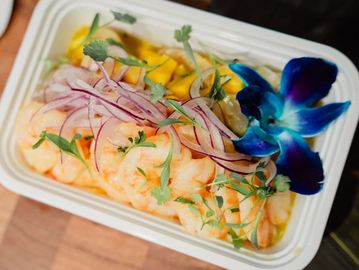 Shrimp dish garnished with herbs, red onions, and a vibrant blue flower.