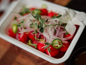 Fresh salad with tomatoes, onions, jalapeños, and herbs in a white container.