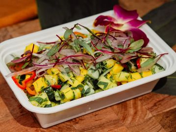 Colorful fresh salad with mango, herbs, and edible flowers in a white tray.