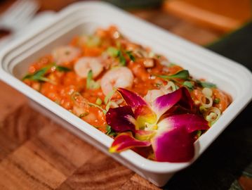 A vibrant shrimp dish garnished with an edible flower in a white container.