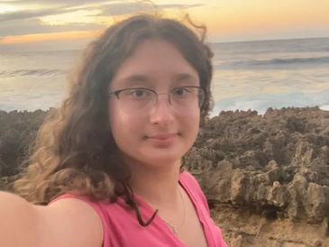 Young woman takes a selfie by rocky shore during sunset.