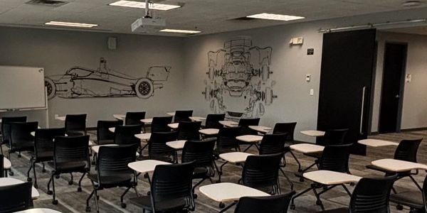 Modern classroom with black chairs and white desks arranged in rows.