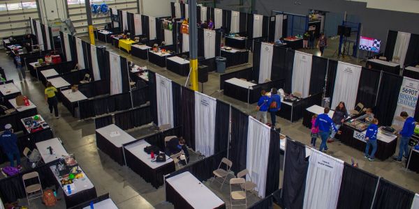 Rows of booths and tables set up in a large indoor event space with few people present.