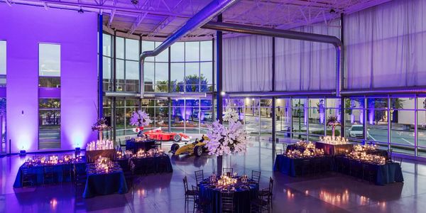 Elegant event setup with race cars and purple lighting in a modern glass venue.