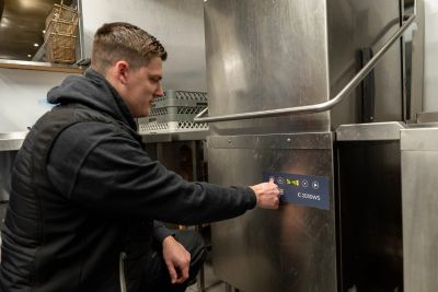 Person operating a commercial dishwasher.