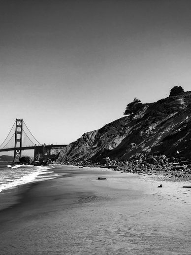 Black and white photo of Golden Gate Bridge from a rocky beach.