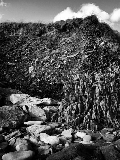 Black and white photo of rocky cliff with grass and clouds.