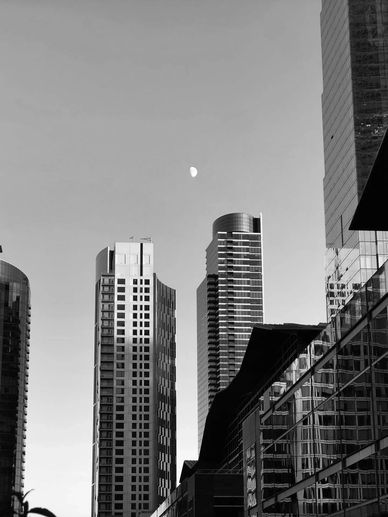 Black and white photo of modern skyscrapers with the moon in the sky.