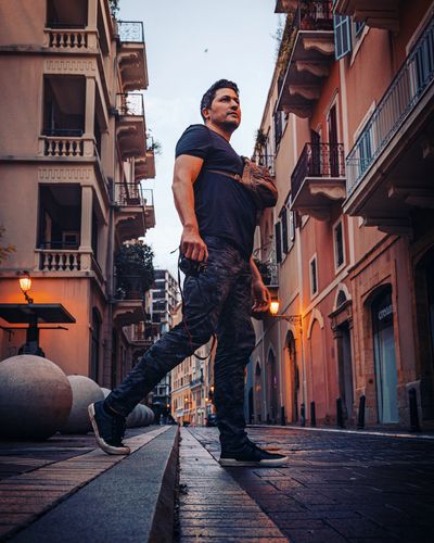 Man walking on a city street holding a camera at dusk.