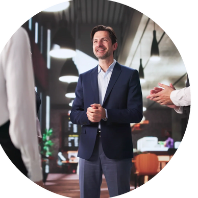 Man in a suit smiling and speaking in a modern office setting.