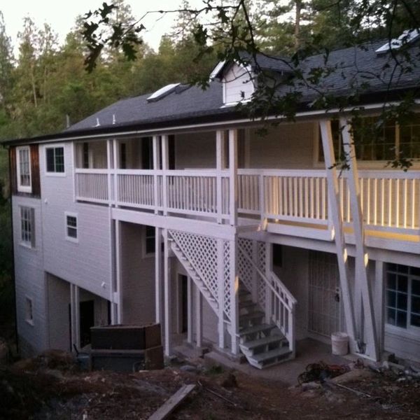 Two-story house with white railings and an outdoor staircase surrounded by trees.
