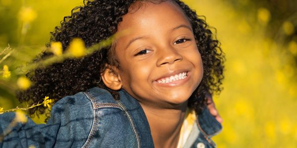 Smiling girl with curly hair in a denim jacket outdoors.
