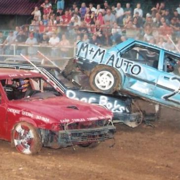 Two damaged cars collide in a demolition derby with a crowd watching.