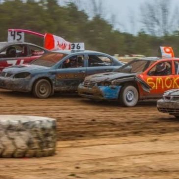 Four dirt track race cars competing closely on a muddy track.