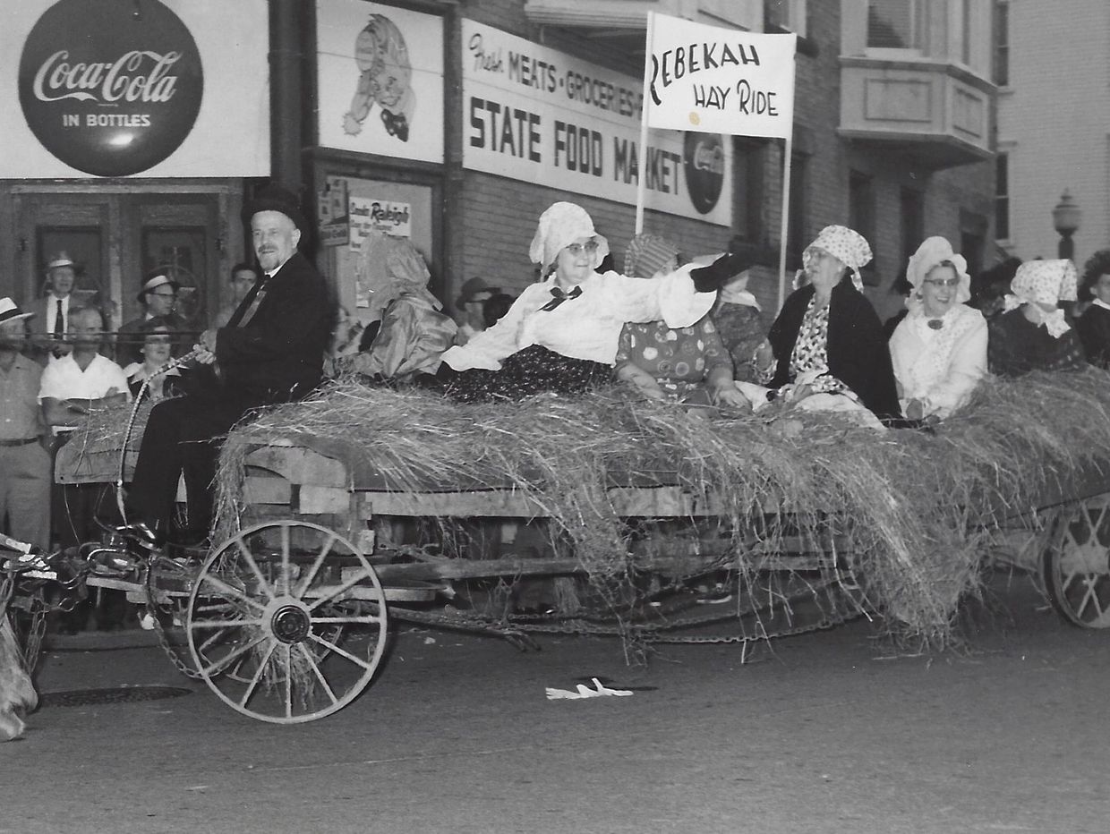 People riding a hay wagon in a parade, holding a sign that says 'Rebekah Hay Ride'.