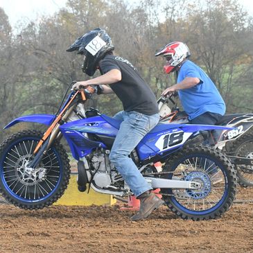 Two riders on blue dirt bikes racing on a dirt track.