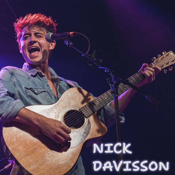 Nick Davisson passionately plays guitar and sings on stage under purple lighting.