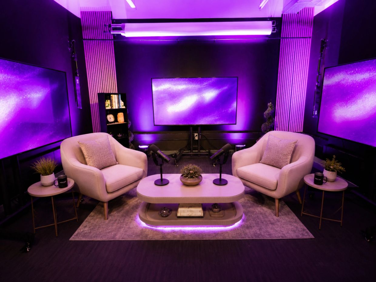 A modern podcast studio with purple lighting and comfy chairs.