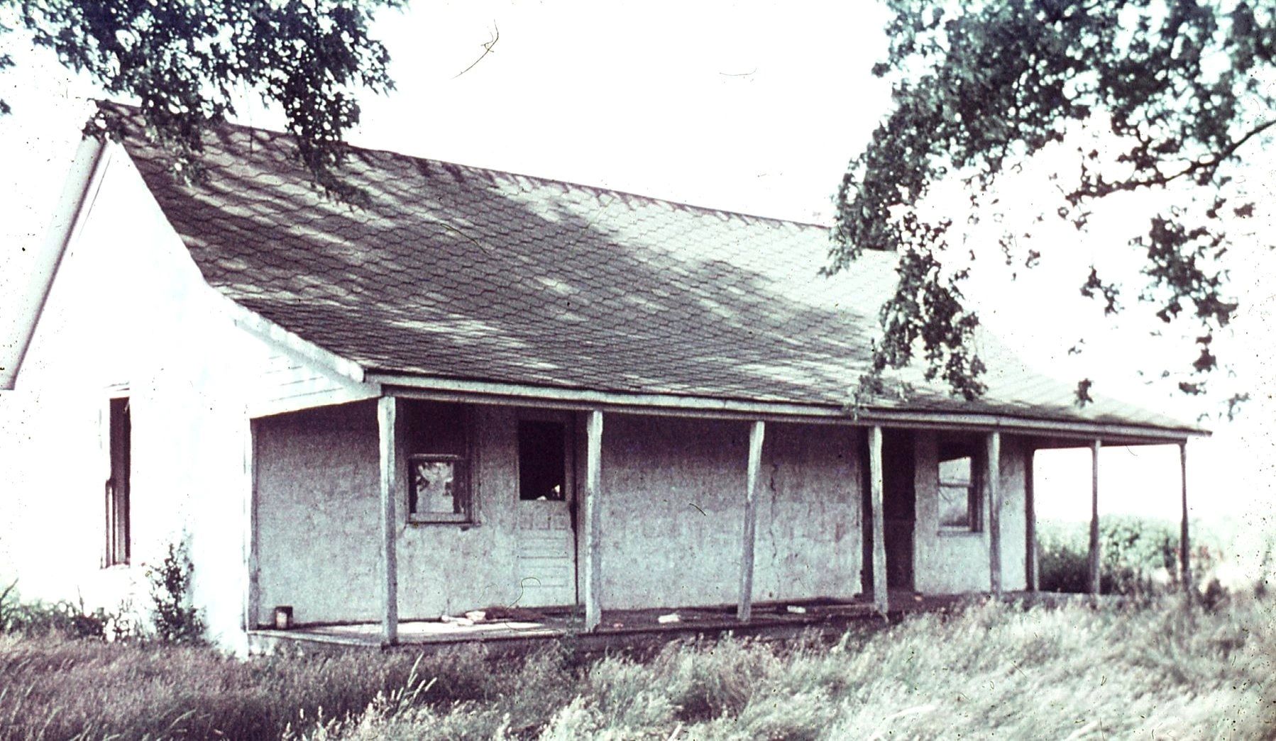 A small, white building with a porch and a grassy area in front of it.
