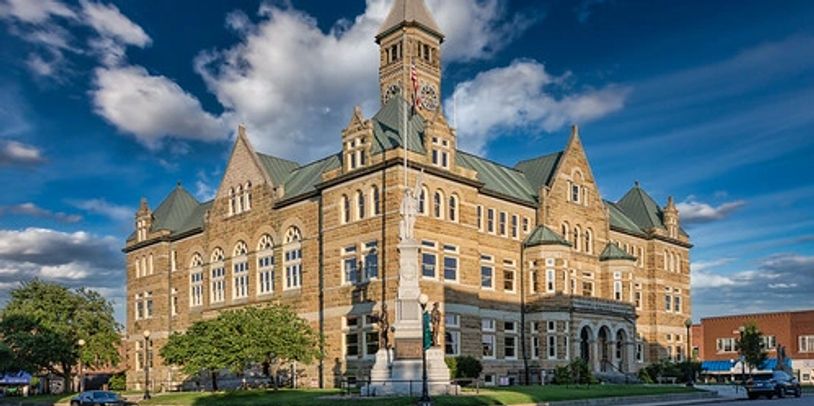 A large, historic stone building with a clock tower and statue in front.